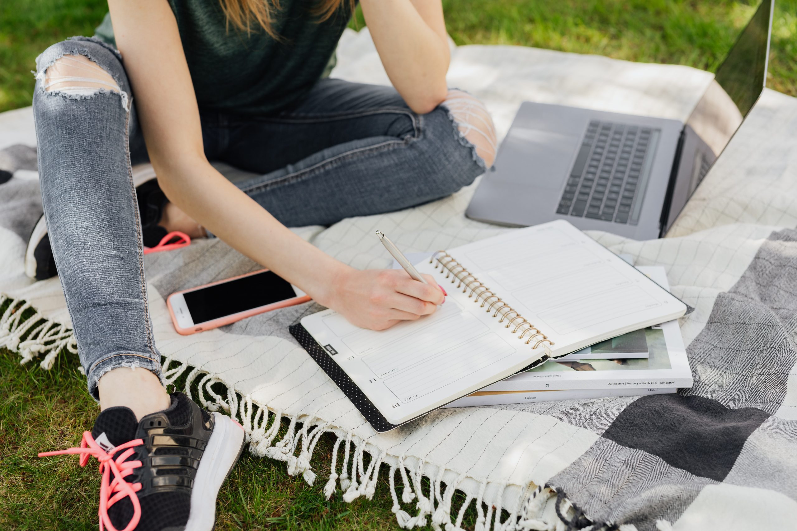 girl with laptop and notepad on blanket in grass