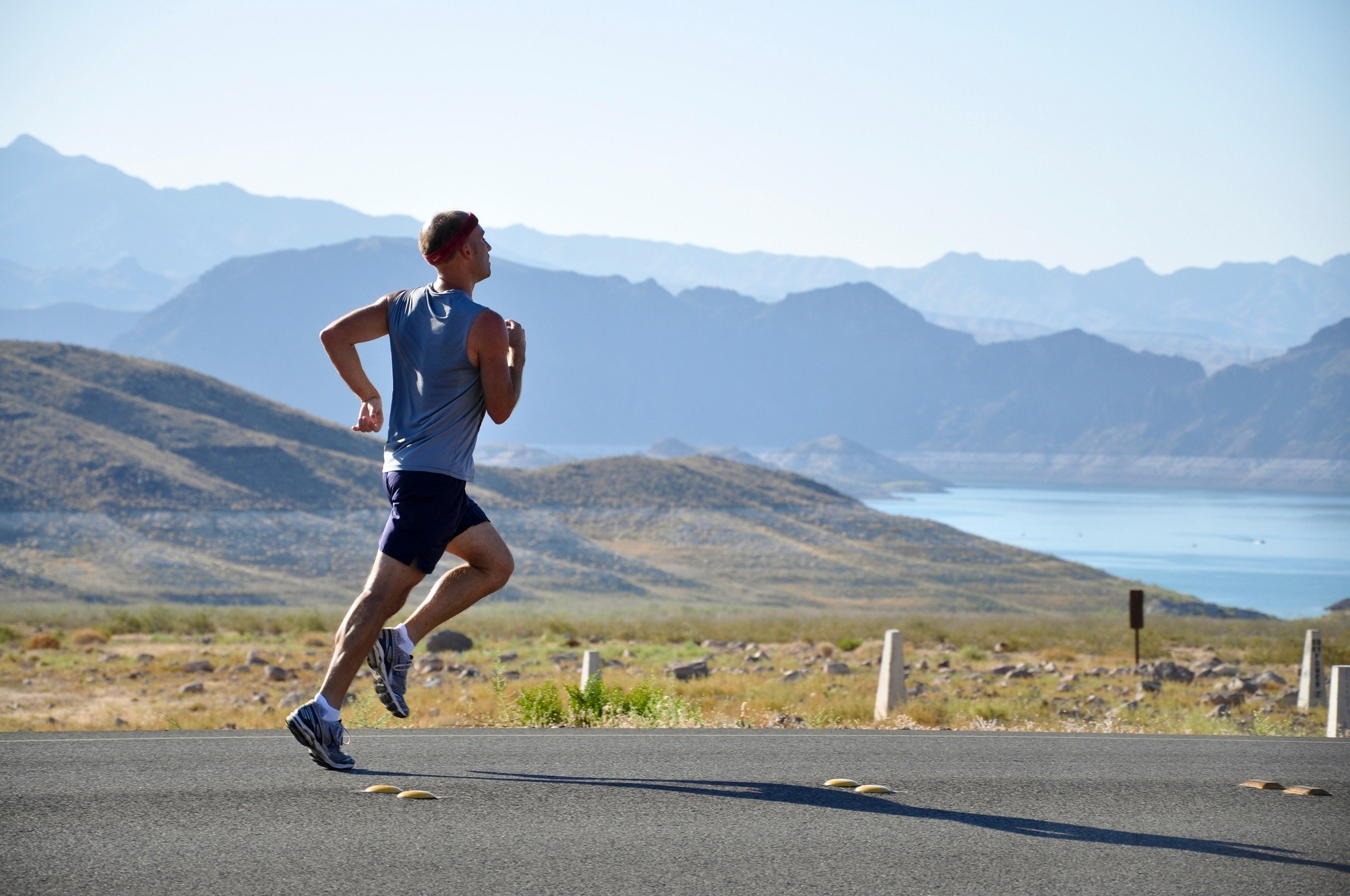 Man running on road by lake and mountains