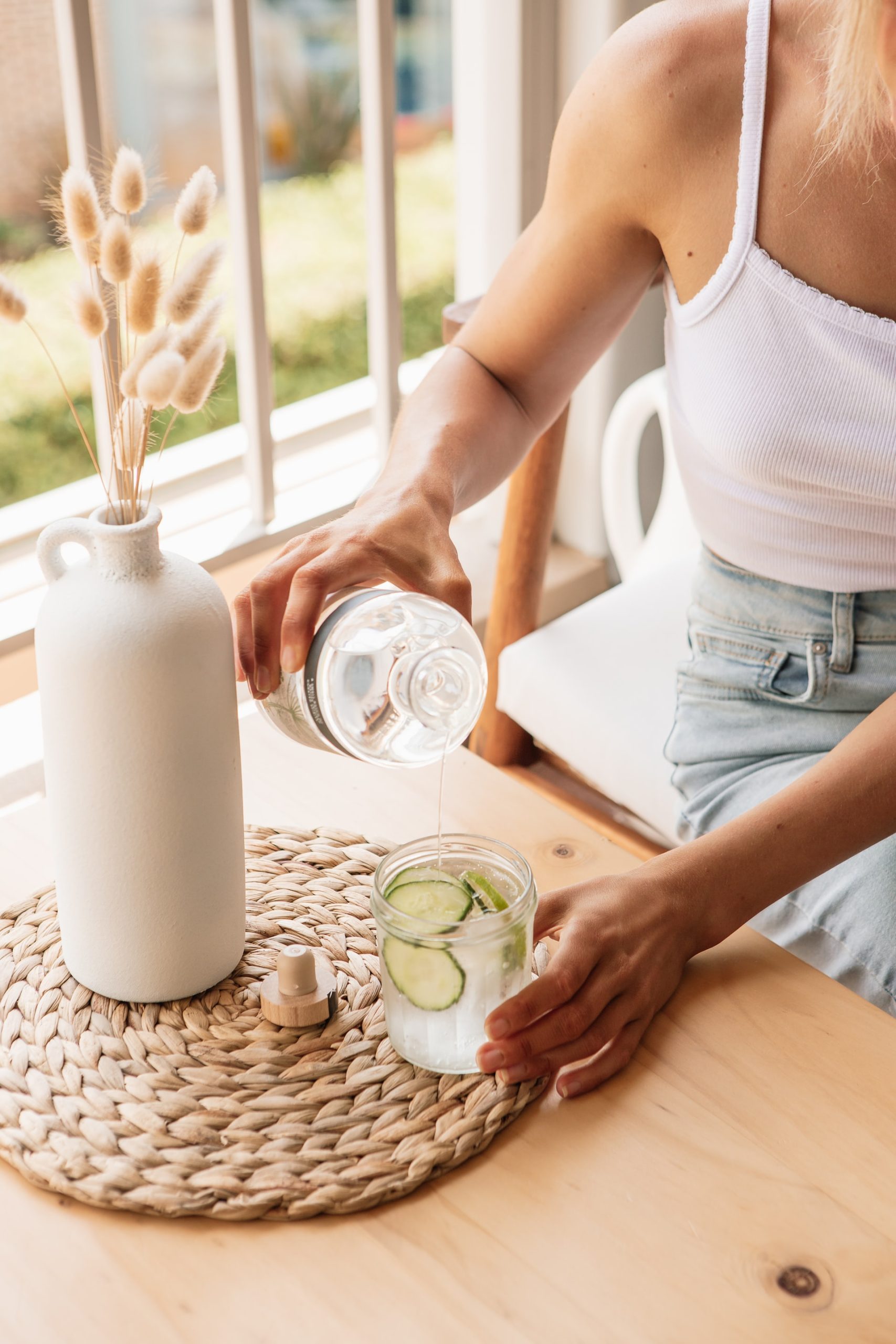 woman pouring cucumber water in glass in kitchen