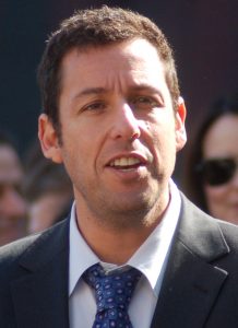 Adam Sandler wearing a suit and tie looking at the camera