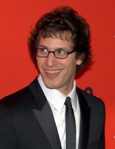 Andy Samberg wearing a suit and tie looking at the camera