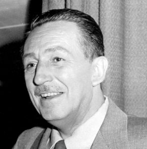 Walt Disney wearing a suit and tie smiling at the camera